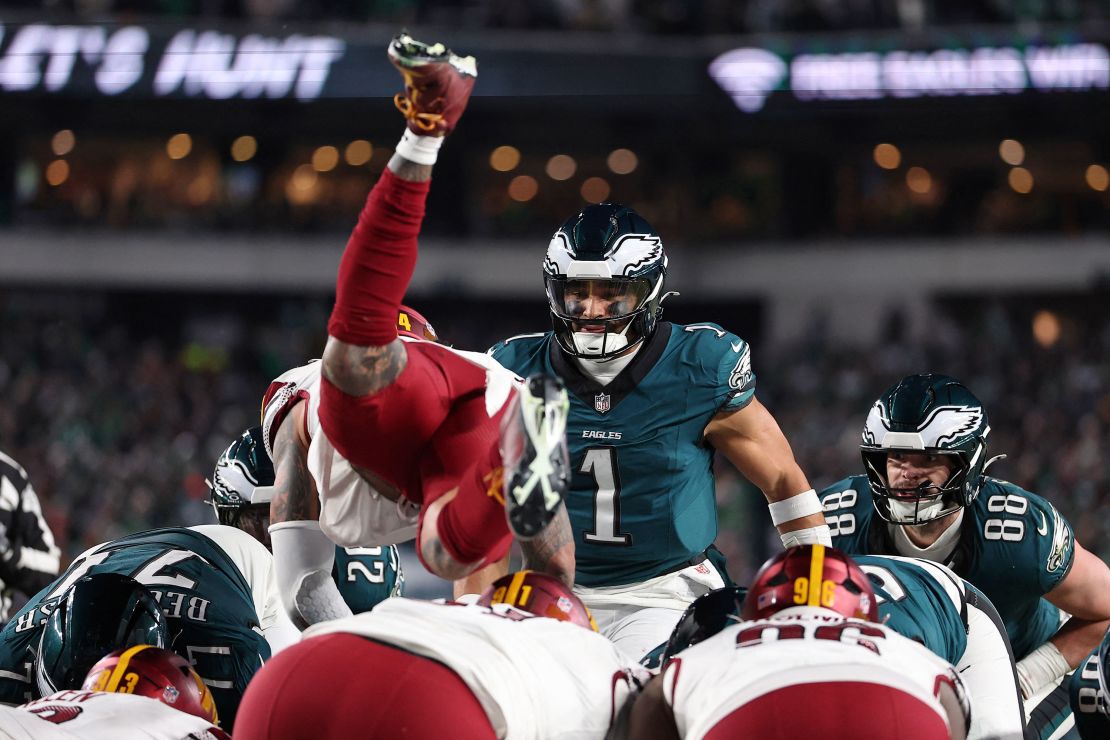 Philadelphia Eagles ⁤quarterback⁤ Jalen Hurts (No. 1) ‌watches as Washington Commanders linebacker Frankie Luvu leaps over the line.