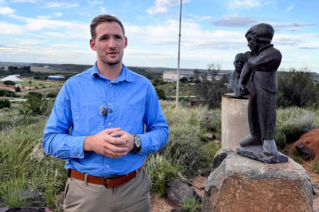 Orania Movement leader Joost Strydom stands next to a symbolic statue of the town, with the town's flag fluttering in the background in Orania, South Africa, on March 31, 2025.