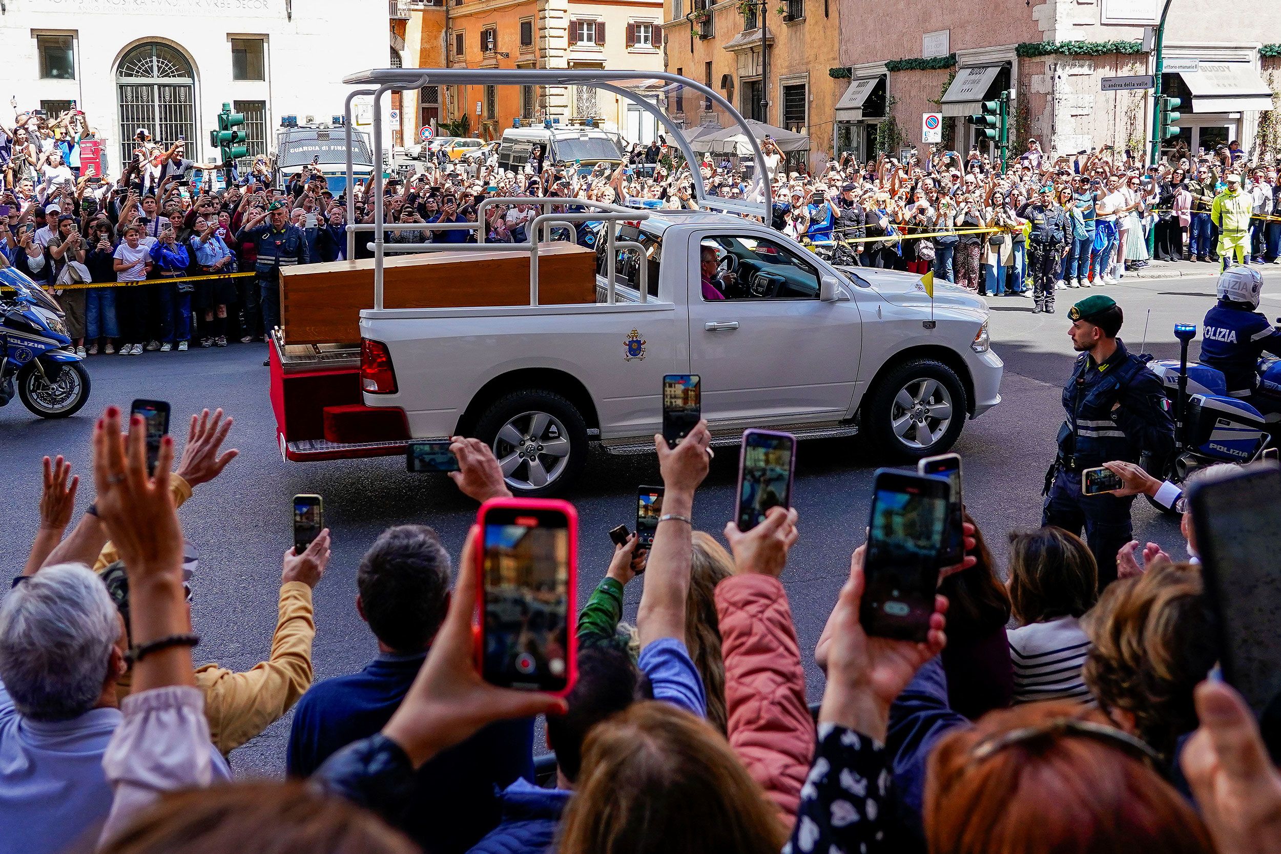 People wave and take pictures with their phones as the coffin of Pope Francis passes by in Rome after his funeral on Saturday, April 26.