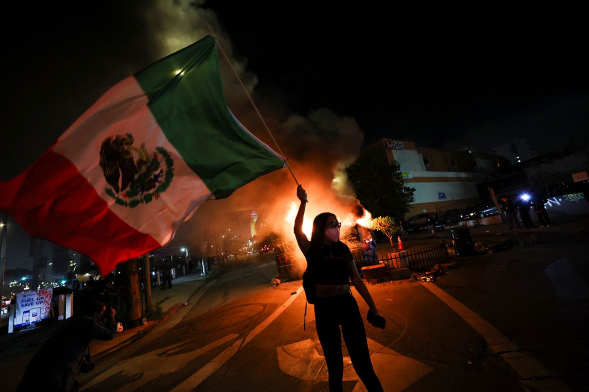 A demonstrator waves a Mexican flag in front of burning dumpsters in downtown Los Angeles on Sunday.