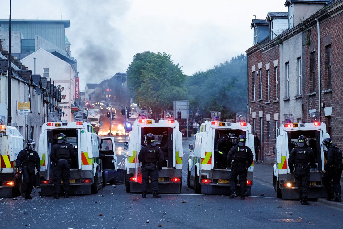 Official vehicles are parked as flames rise during a second night of riots, in Ballymena, Northern Ireland, on June 10, 2025.