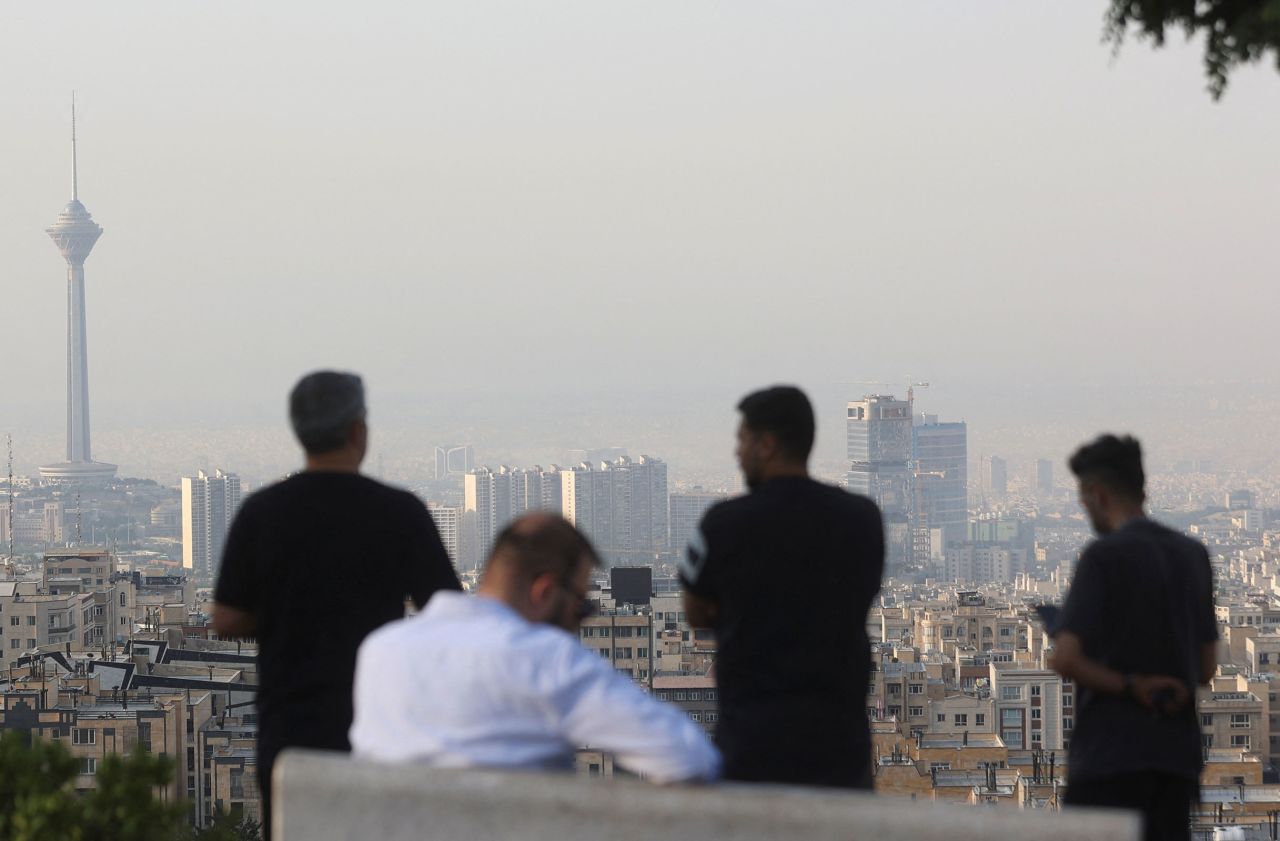 مردانی که پس از حملات اسرائیل در روز جمعه، چشم‌انداز شهری تهران را مشاهده می‌کنند.