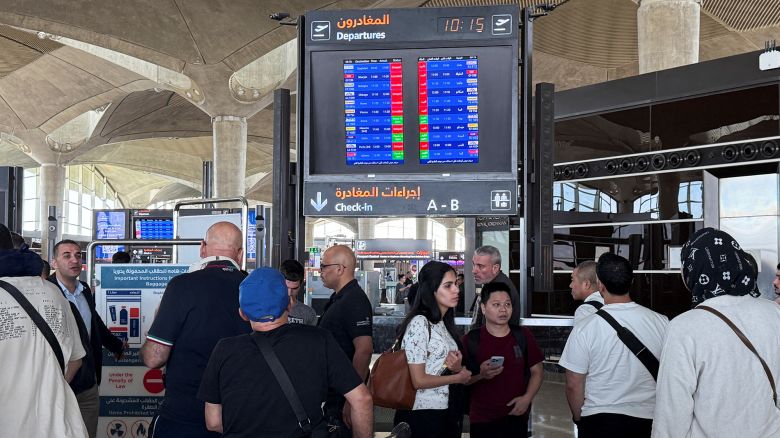 People stand in front of a flight information display screen showing information about delayed and cancelled flights, at Queen Alia International Airport in Amman, Jordan.