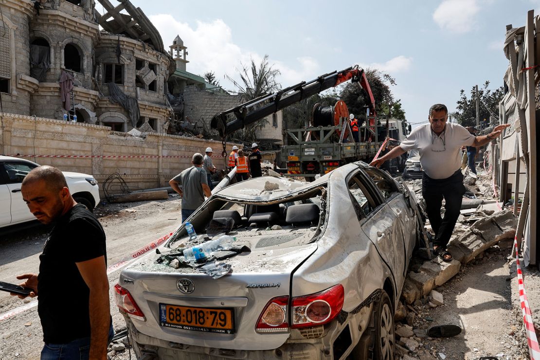 Men walk near a damaged vehicle at an impact site following missile attack from Iran in Tamra, northern Israel, on June 15, 2025.