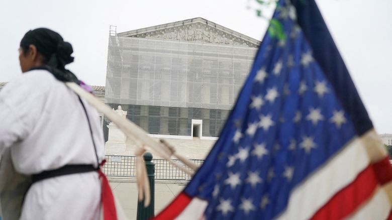 A person stands with a US flag attached to them, after the Supreme Court dealt a blow to the power of federal judges by restricting their ability to grant broad legal relief in cases outside the court in Washington, D.C., on June 27, 2025.