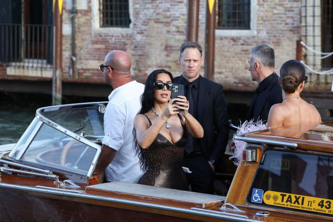 Kim Kardashian takes a photo as she rides a taxi boat to the wedding on Friday.