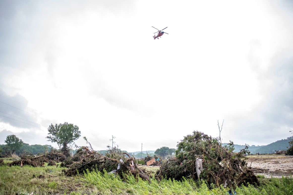 A helicopter flies overhead as volunteers search for flood victims in Kerr County.