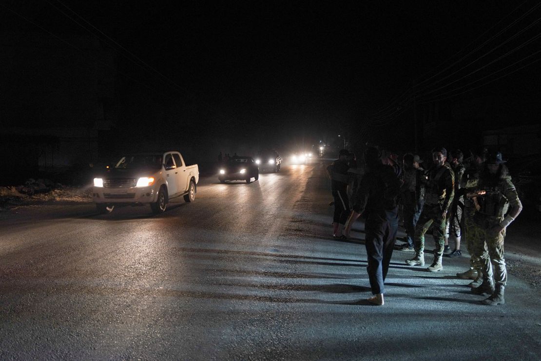 Members of Syrian security forces stand on the side of a road as vehicles transporting other Syrian security forces make their way out of the predominantly druze city of Suwayda.