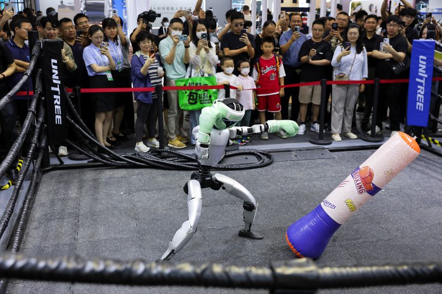 People watch a humanoid robot play boxing at a Unitree booth during the World Artificial Intelligence Conference in Shanghai, China July 26, 2025.