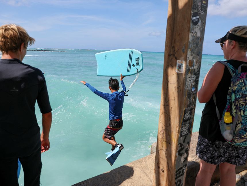 A bodyboarder jumps into water off Waikiki Beach after authorities downgraded earlier tsunami warnings.