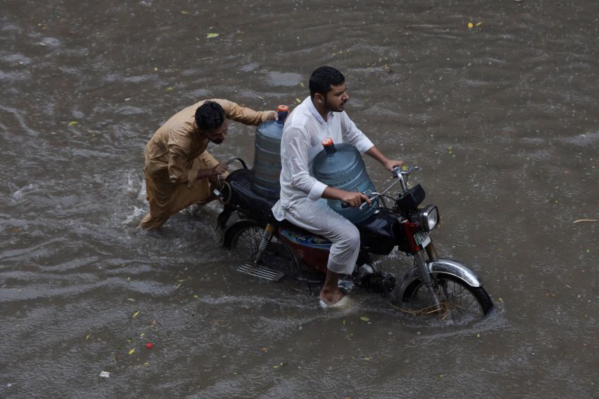 Men transport water bottles on a motorbike through a flooded street amid a downpour in Lahore, Pakistan August 9, 2025.