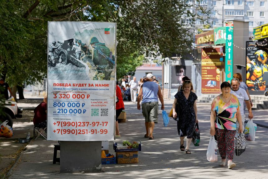People walk past a banner promoting a contract military service in the Russian armed forces in the city of Melitopol in the Zaporizhzhia region, a Russian-controlled area of Ukraine.