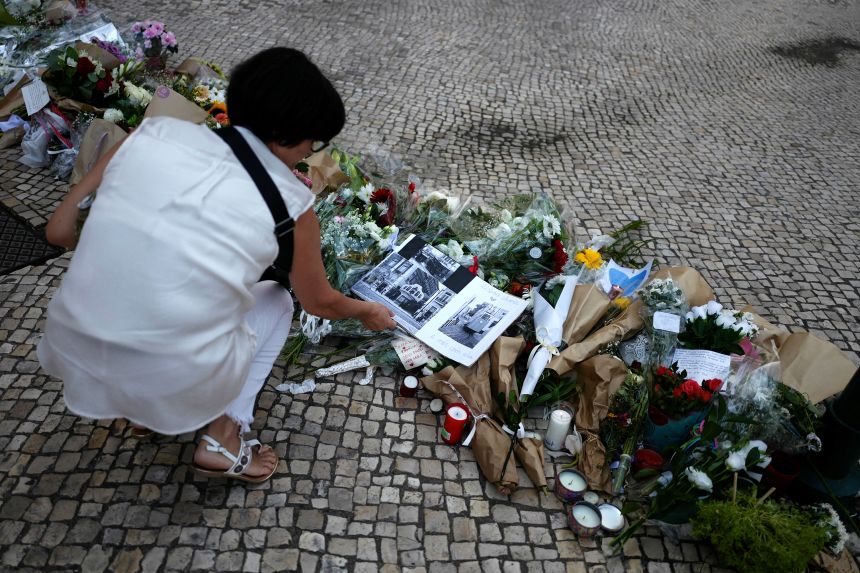 A woman sits next to a makeshift memorial honoring the victims of the funicular crash on Friday.