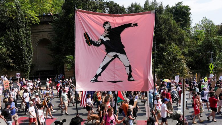 Demonstrators hold a banner in the style of the artist Banksy, showing a masked protester throwing a sandwich, as they attend a "We Are All DC" march, in Washington, DC, on September 6, 2025. The image of a man throwing a sandwich, inspired by a man who threw a sandwich at a Border Patrol officer, became a protest symbol during Trump's crackdown on crime in the nation's capital.