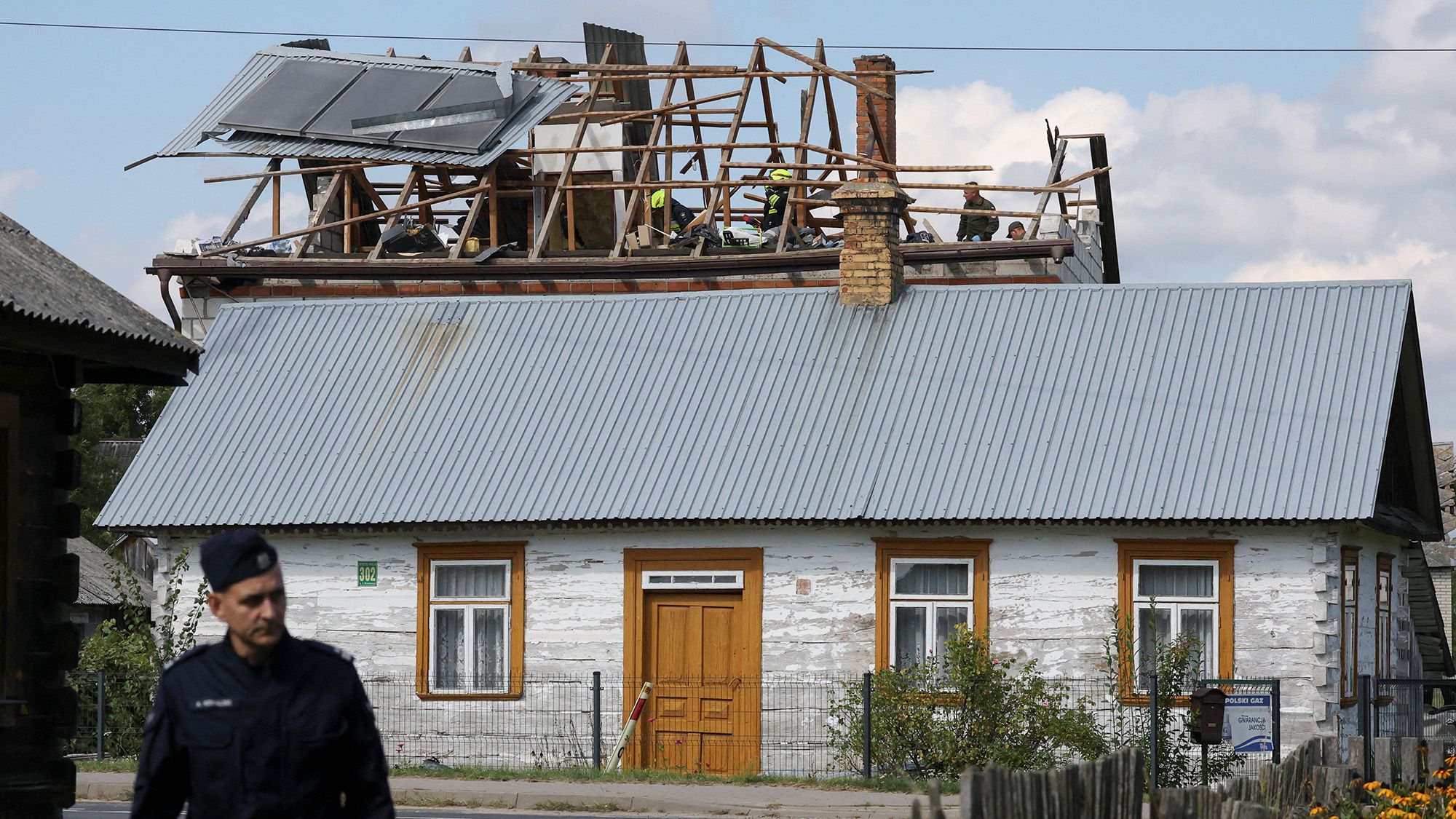 A police officer stands below as firefighters work on the destroyed roof of a house, after Russian drones violated Polish airspace during an attack on Ukraine, with some being shot down by Poland with the backing from its NATO allies, in Wyryki, Lublin Voivodeship, Poland, September 10, 2025. REUTERS/Kacper Pempel    