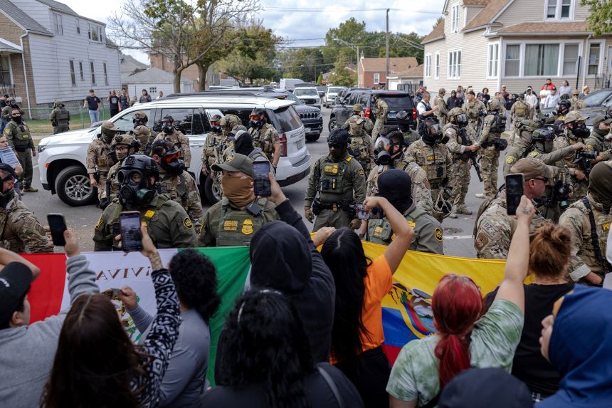 Federal agents stand guard as community members gather near a car crash site in Chicago on Tuesday, October 14.