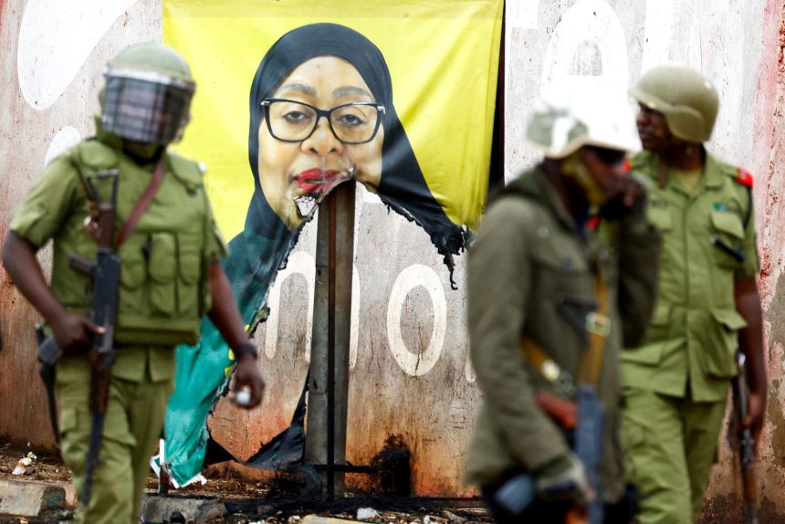 Tanzanian riot police officers walk past a vandalised campaign poster of President Samia Suluhu Hassan following demonstrations on Thursday.