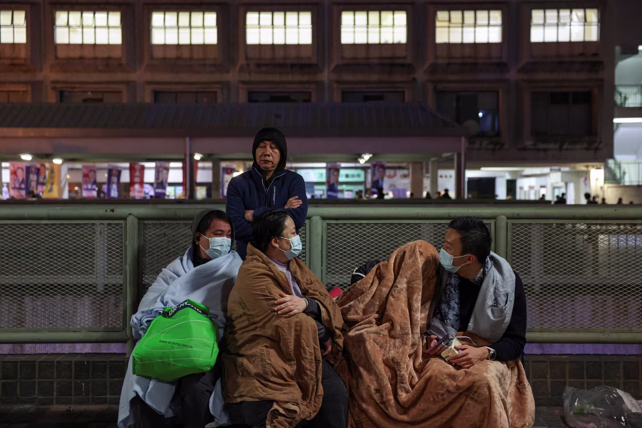 Evacuees wrapped in blankets rest on a platform near the site of a major fire at Wang Fuk Court housing estate in Tai Po, Hong Kong, on Wednesday.