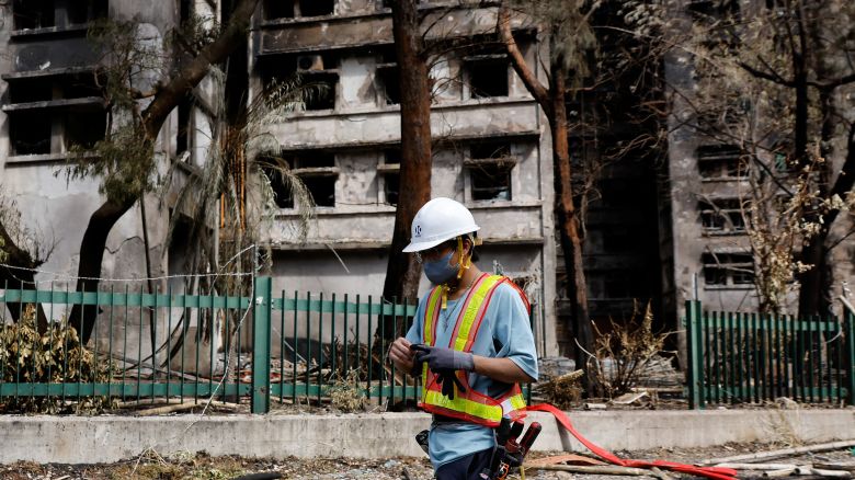 A repair worker walks past burnt buildings after the deadly fire at the Wang Fuk Court housing complex, in Tai Po, Hong Kong, on November 29, 2025.