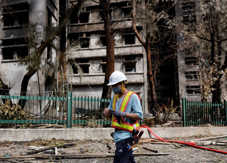 A repair worker walks past burnt buildings after the deadly fire at the Wang Fuk Court housing complex, in Tai Po, Hong Kong, on November 29, 2025.