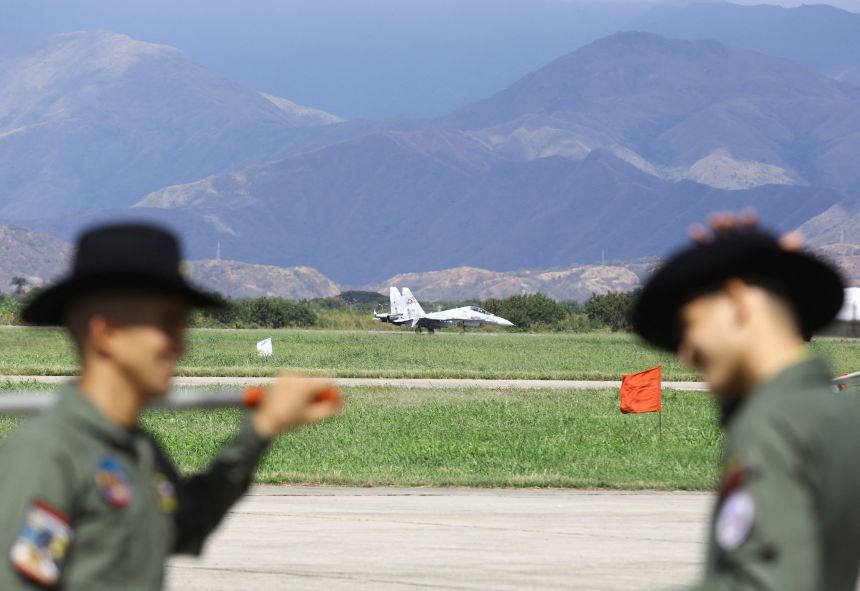 Soldiers talk as a military plane is seen in the background during the Expo Aeronautica Venezuela 2025, after US President Donald Trump said on Saturday the airspace above and surrounding Venezuela should be considered 