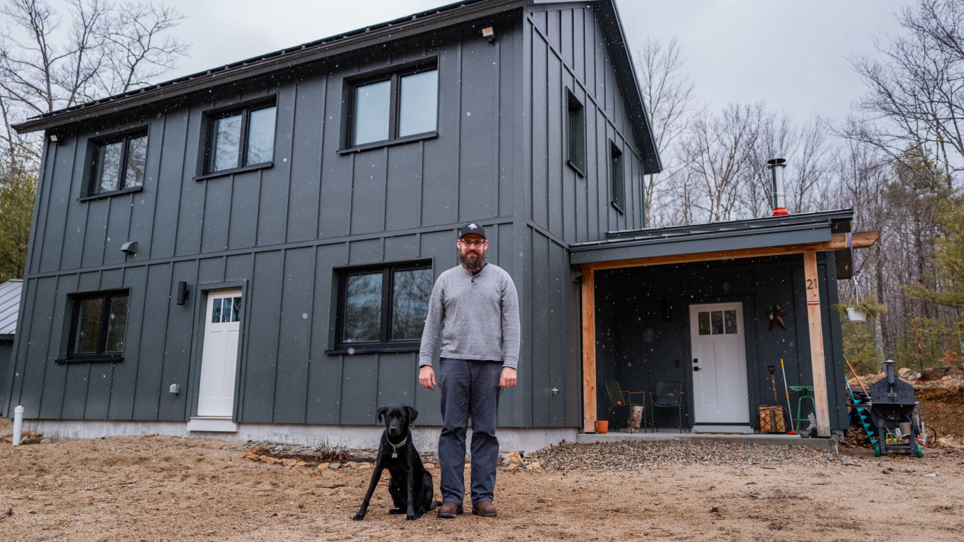 Colin Goodson and his dog outside his off-the-grid home in Maine, powered by solar and batteries.