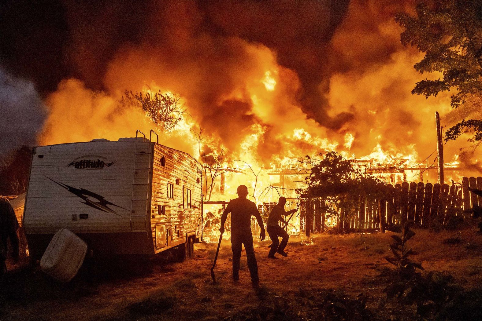 People work to stop flames at a burning home from spreading to a neighboring house as the 6-5 Fire burns through the small town of Chinese Camp, California, on Tuesday, September 2. <a href="index.php?page=&url=https%3A%2F%2Fwww.cnn.com%2F2025%2F09%2F03%2Fweather%2Fcalifornia-wildfire-chinese-camp-mining-town-hnk">The wildfire</a> damaged and destroyed multiple buildings after igniting in a lightning storm.