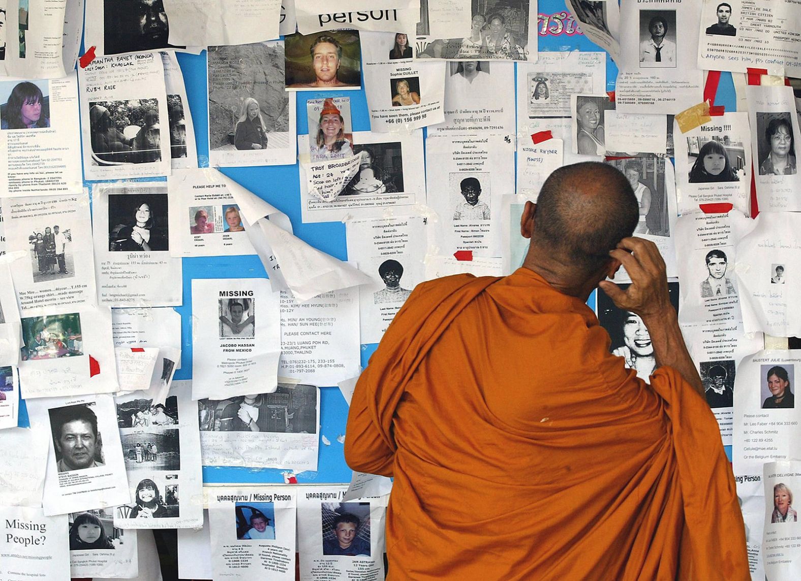 A Buddhist monk looks at notices of missing persons displayed at a hospital in Phuket, Thailand.