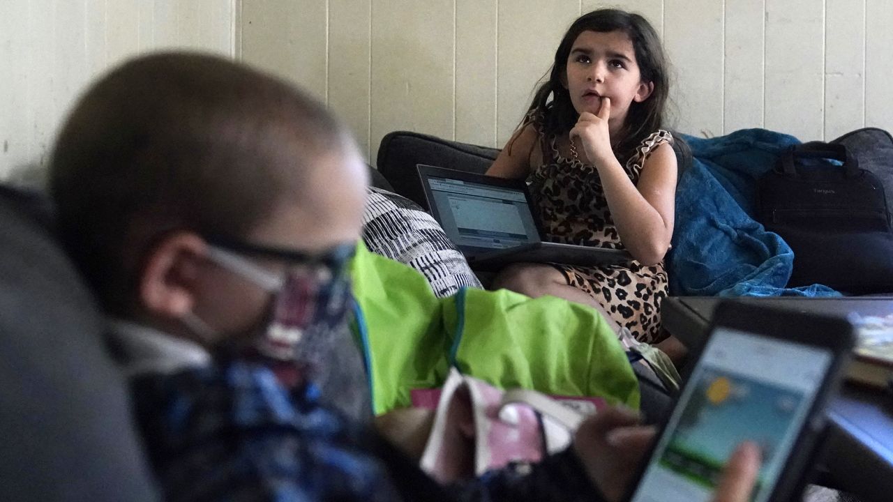 Third grader Elena recites multiplication tables as her brother Wyatt reviews his kindergarten work on a tablet with their mom, Christi Brouder, in Haverhill, Massachusetts.