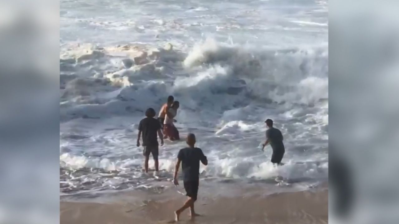 Wright holds onto the unidentified woman in the water to prepare for an oncoming wave as they make their way to shore.