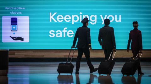 This picture taken on September 29, 2020 shows Qatar Airlines flight crew members walking past an illuminated sign displaying a message relating to the COVID-19 novel coronavirus at the Sydney International Airport in Sydney. (Photo by David GRAY / AFP) (Photo by DAVID GRAY/AFP via Getty Images)