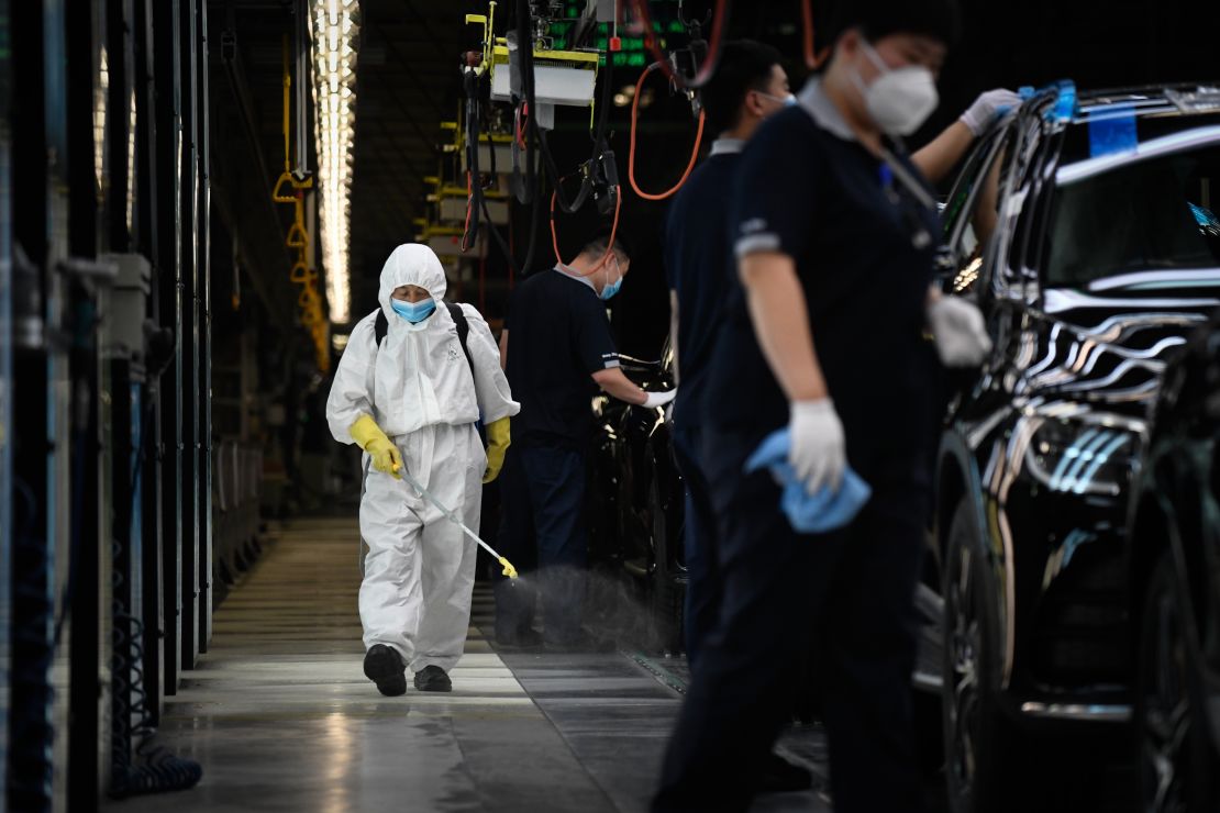 A cleaner wearing protective gear sprays disinfectant along a production line at an automotive plant in Beijing on May 13, 2020.