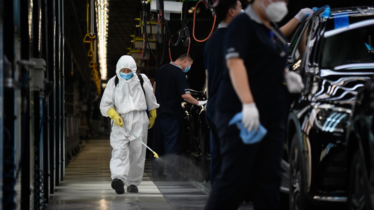 A cleaner wearing protective gear sprays disinfectant along a production line at an automotive plant in Beijing on May 13, 2020.