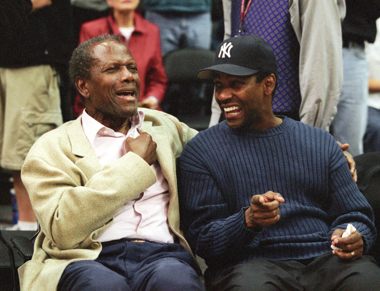 Poitier laughs with actor Denzel Washington at an NBA playoff game in Los Angeles in 2002.