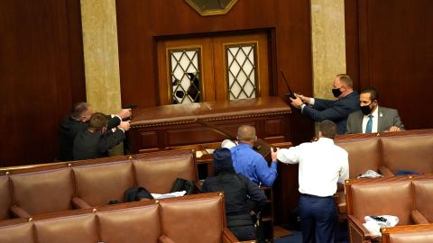 Law enforcement officers point their guns at a door that was vandalized in the House Chamber. 
