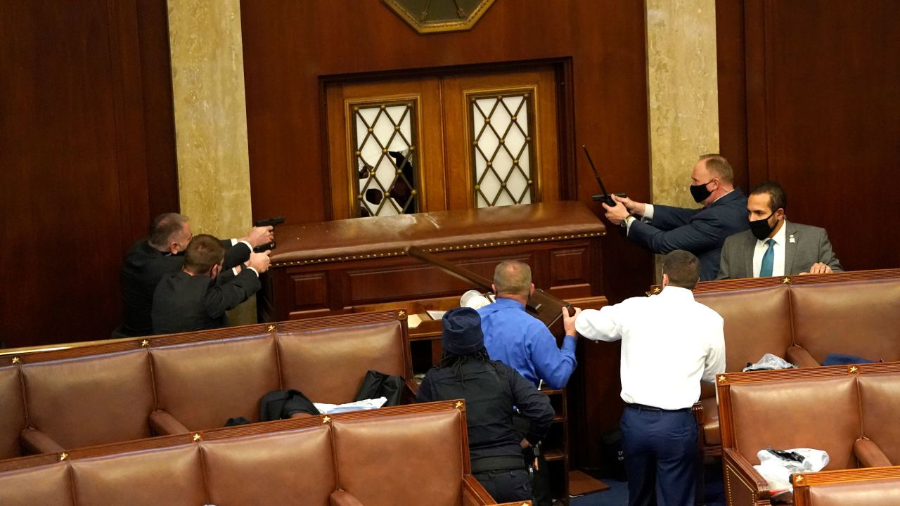 Law enforcement officers point their guns at a door that was vandalized in the House Chamber.
