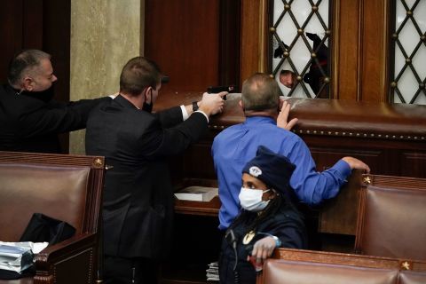 Law enforcement officers point their guns at a door that was vandalized in the House chamber after the Capitol was breached.