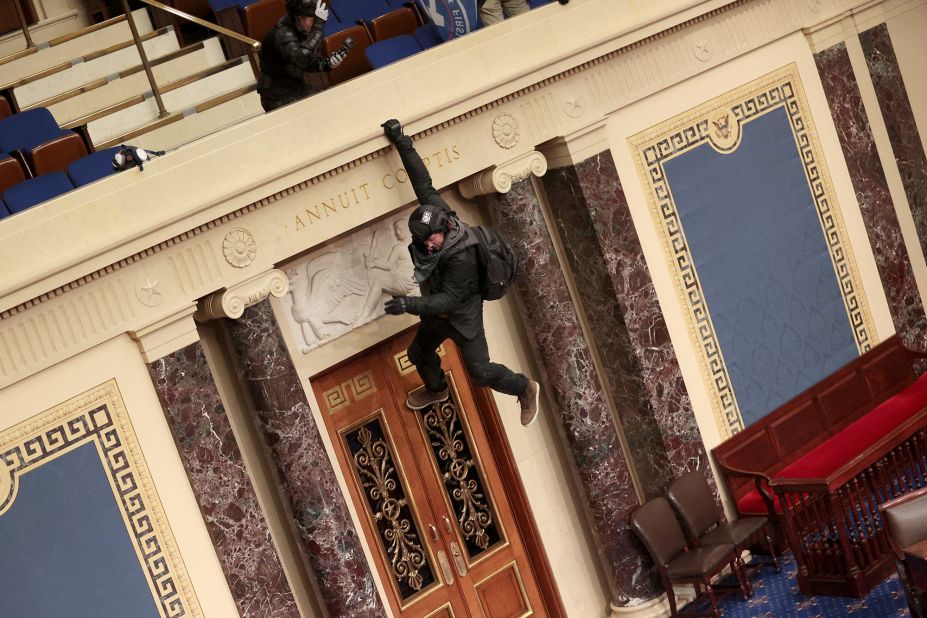 A rioter hangs from a balcony in the Senate chamber.
