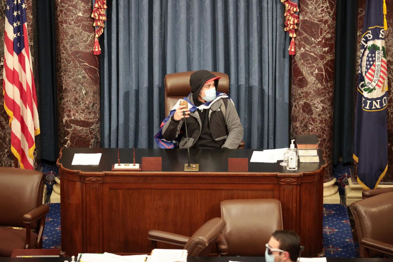 A rioter sits in the Senate chamber.