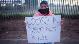 TOPSHOT - A woman holds up a placard as a small group of people take part in a protest outside a school in Bishop Lavis, to protest against the South African government's decision to open some schools, in Cape Town on June 1, 2020. - South Africa moved into level three of a five-tier lockdown on June 1, 2020, to continue efforts to curb the spread of the COVID-19 coronavirus. Under level three, all but high-risk sectors of the economy will be allowed to reopen.There are however a lot of confusion around the reopening of schools as some schools have opened and others remain closed. (Photo by RODGER BOSCH / AFP) (Photo by RODGER BOSCH/AFP via Getty Images)