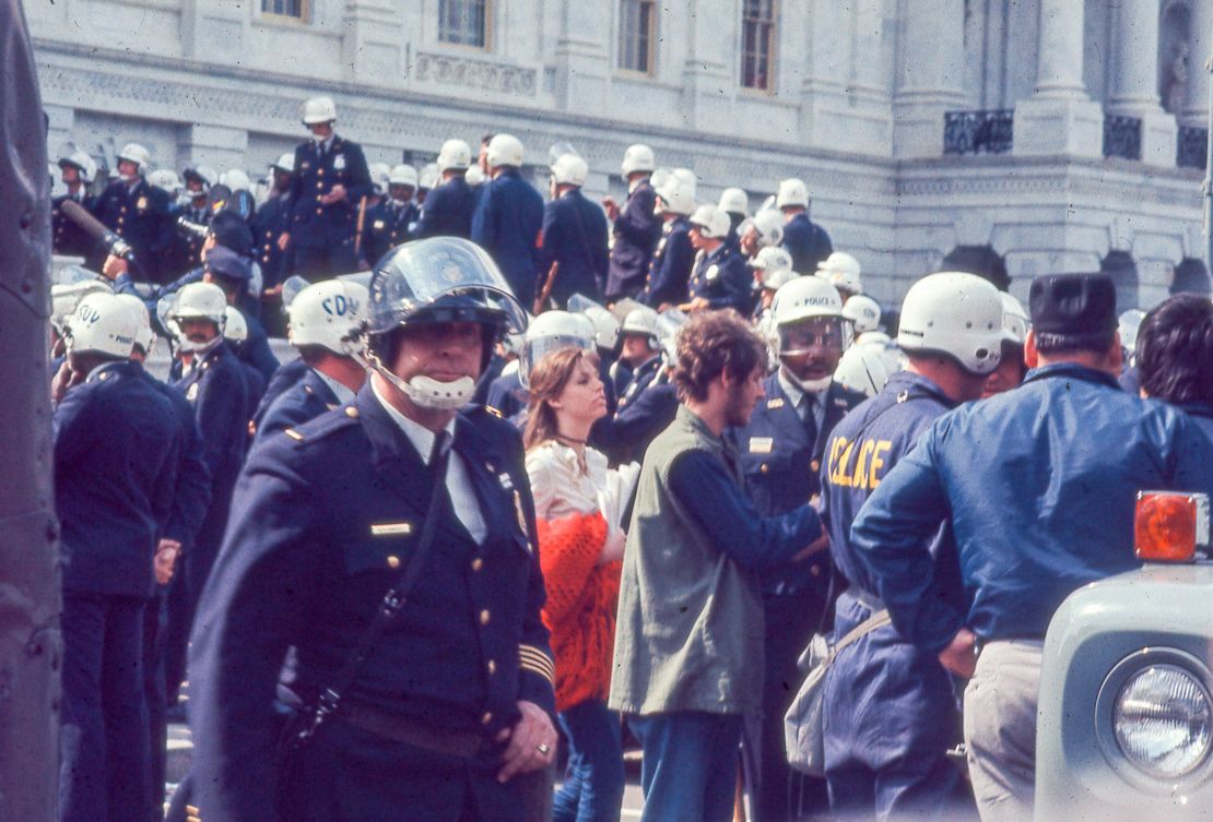 Police in riot gear surround protesters in hippie attire during the 1971 May Day protests.