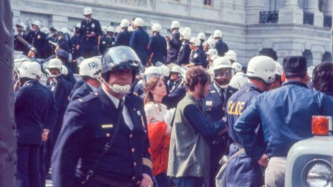 Police in riot gear surround protesters in hippie attire during the 1971 May Day protests.