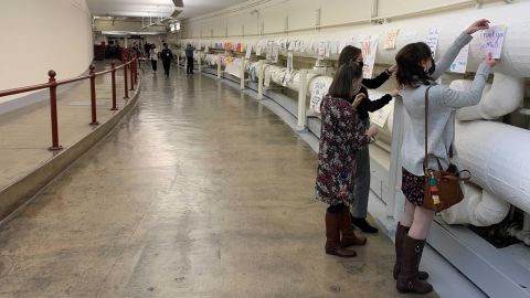 Three women tape signs thanking US Capitol Police officers in a tunnel toward the House of Representatives in the wake of the January 6 attack.
