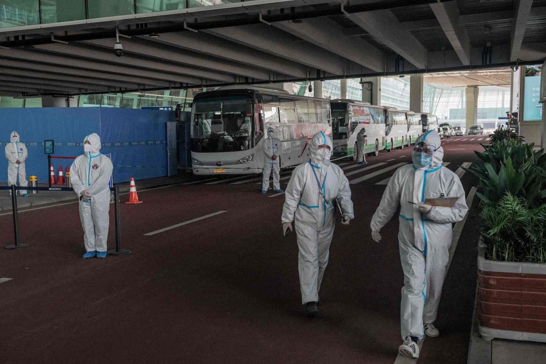 Health workers stand next to buses at a cordoned-off section, where arriving travellers are to be taken into quarantine, at the internatinoal airport in Wuhan, China on January 14, 2021, following the arrival of a World Health Organization (WHO) team investigating the origins of the Covid-19 pandemic.