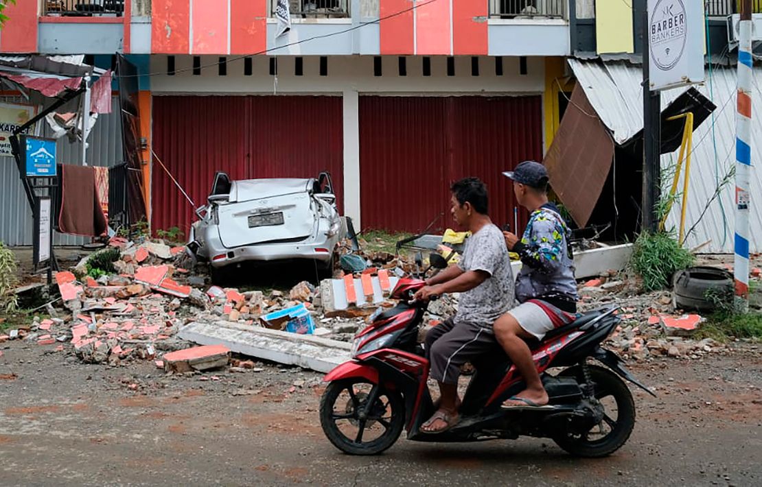 Motorists ride past the wreckage of a car damaged in an earthquake in Mamuju, West Sulawesi, Indonesia.