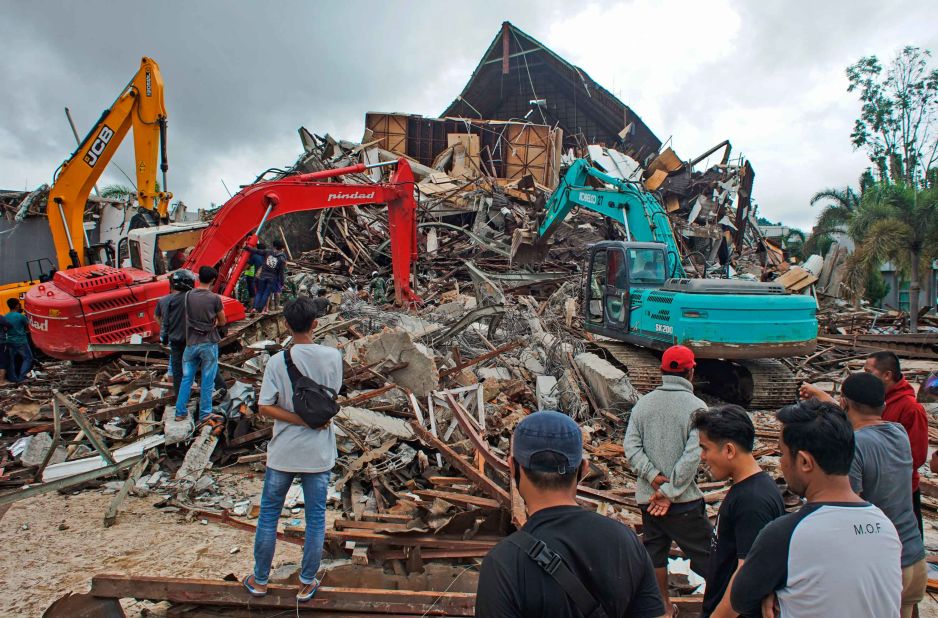 People look on as members of the emergency services work at the site of a government building that collapsed during the earthquake in Mamuju.