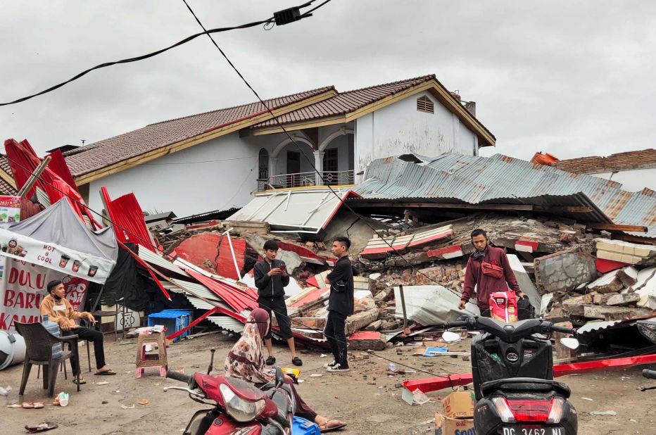 Residents stand near a structure that was flattened by the earthquake in Mamuju.