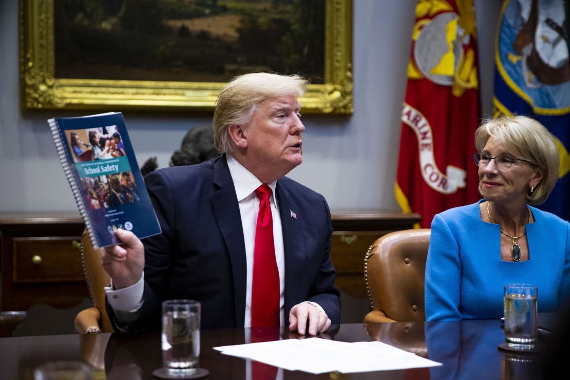 Trump holds up the Federal Commission on School Safety report while Betsy DeVos, U.S. secretary of education, right, listens. 