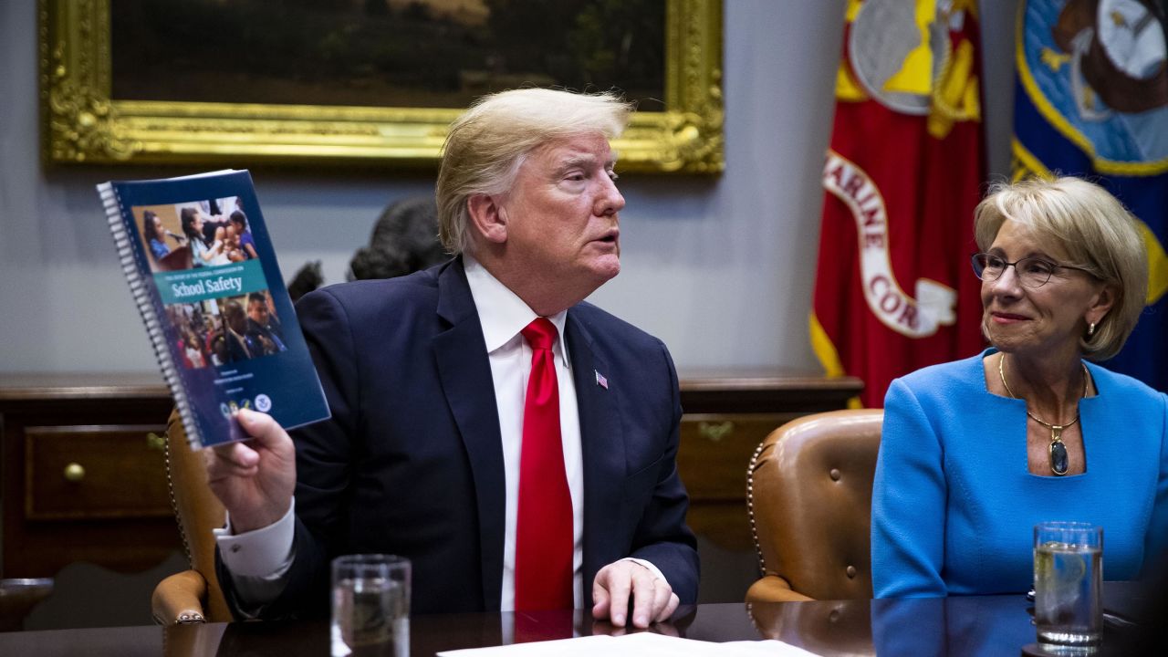 Trump holds up the Federal Commission on School Safety report while Betsy DeVos, U.S. secretary of education, right, listens.