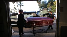 EL CAJON, CALIFORNIA - JANUARY 15: (EDITORIAL USE ONLY) Embalmer and funeral director Kristy Oliver (L) and funeral attendant Sam Deras load the casket of a person who died after contracting COVID-19 into a hearse at East County Mortuary on January 15, 2021 in El Cajon, California. The mortuary on average was handling about 50 bodies per month but owner Robert Zakar believes they may process closer to 100 in January as California continues to see a spike in coronavirus deaths. The mortuary holds the bodies of those who pass away due to COVID-19 for a minimum of three days before they are processed along with various other COVID-related safety measures.  (Photo by Mario Tama/Getty Images)